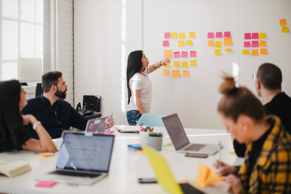 Workshopbegeleider wijst naar memoblaadjes op een whiteboard voor een groep